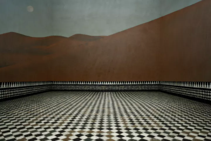 Chambre des Rêves 008 Une grande pièce vide au carrelage en damier. Projetée sur les murs, une image de désert.