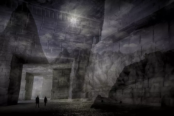 Déambulant dans une salle démesurée dont les parois représentent un paysage montagneux, deux silhouettes d'hommes nous semblent infimes.